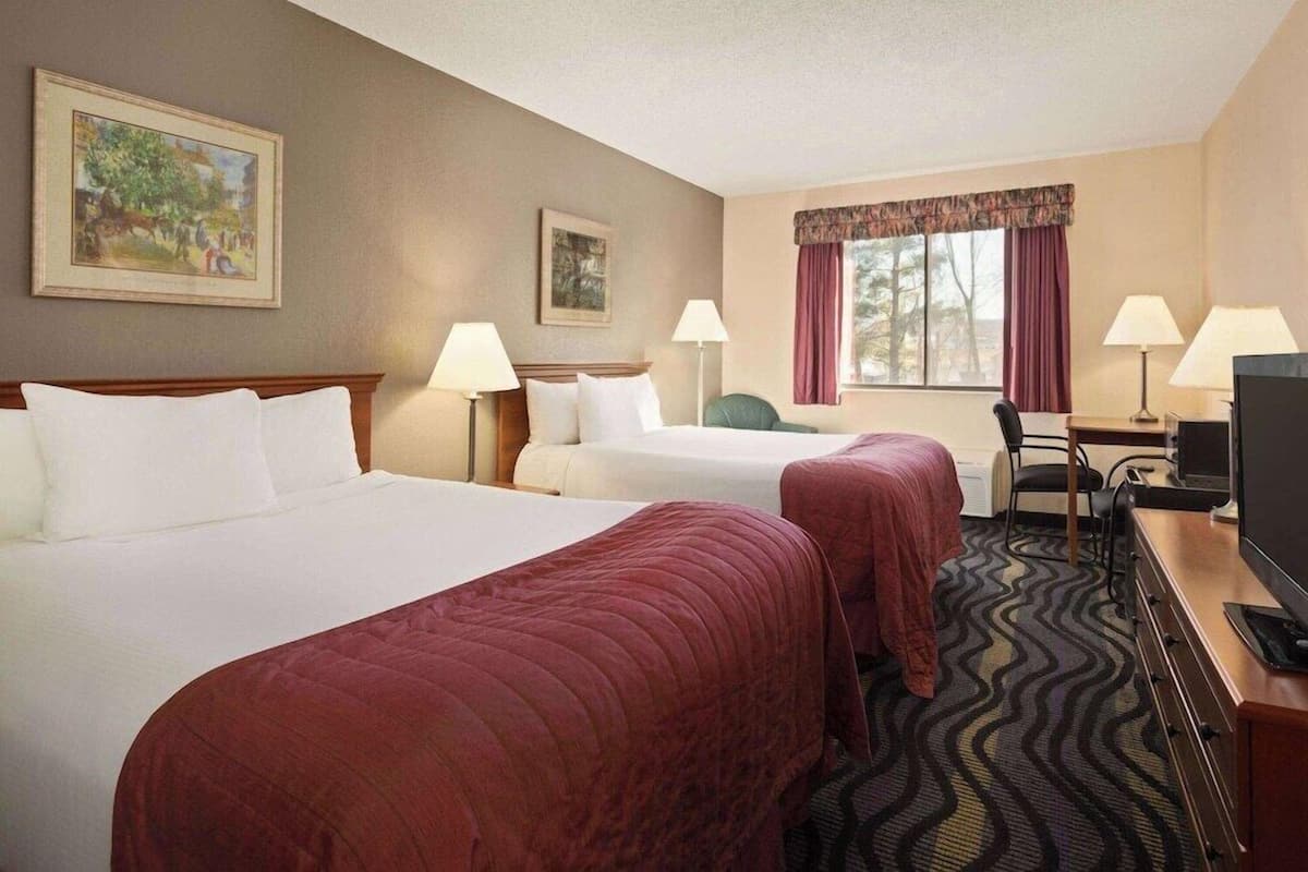 A hotel room with two beds, a desk with a television, and two lamps.