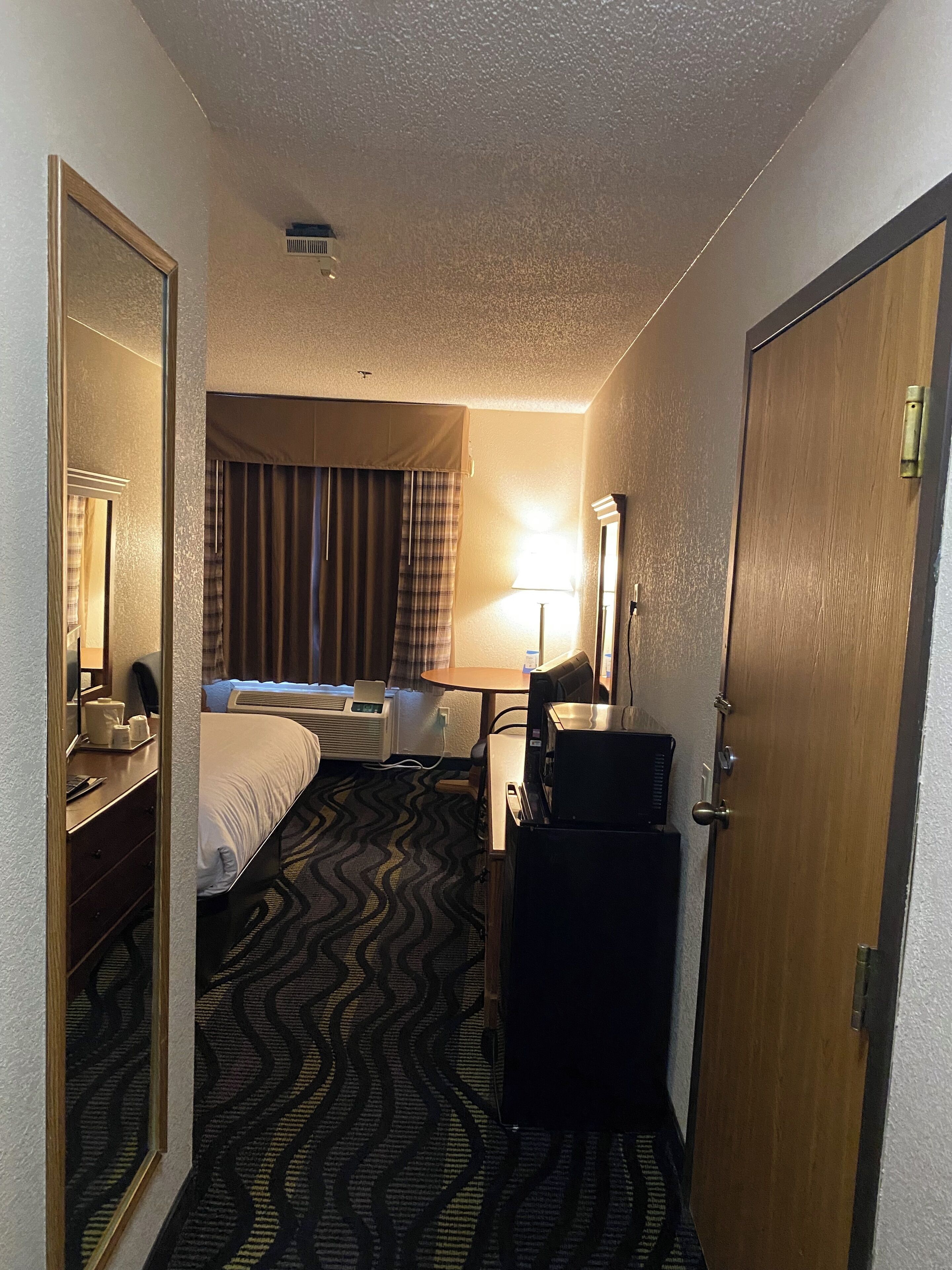 A hotel room with a bed, a desk, a chair, a lamp, and a minibar.