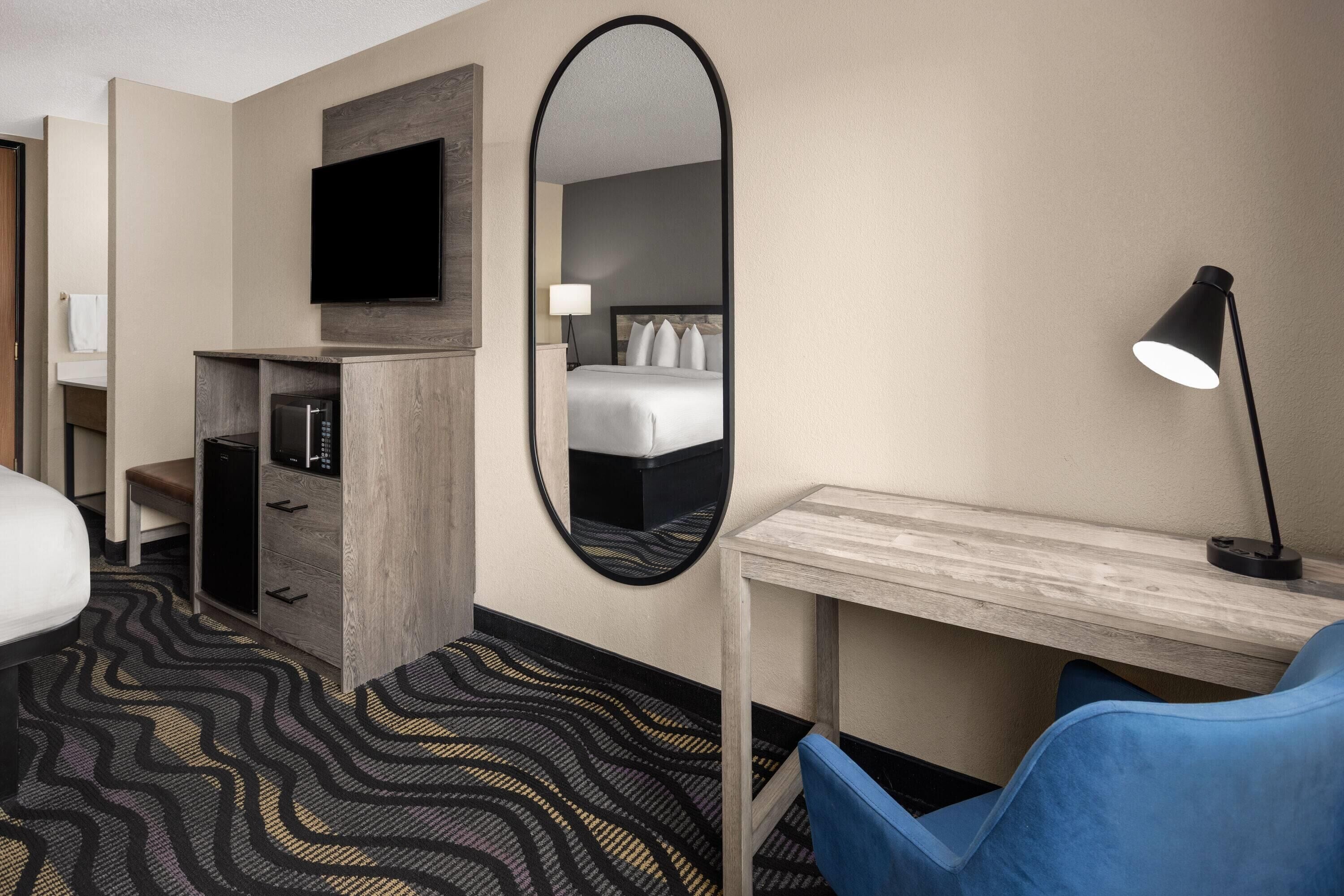 Een hotelkamer met een bed, een bureau, een stoel, een televisie, een spiegel en een lamp.