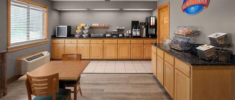 A kitchen with wooden cabinets, a dining table with chairs, a ceiling fan, and a breakfast sign.