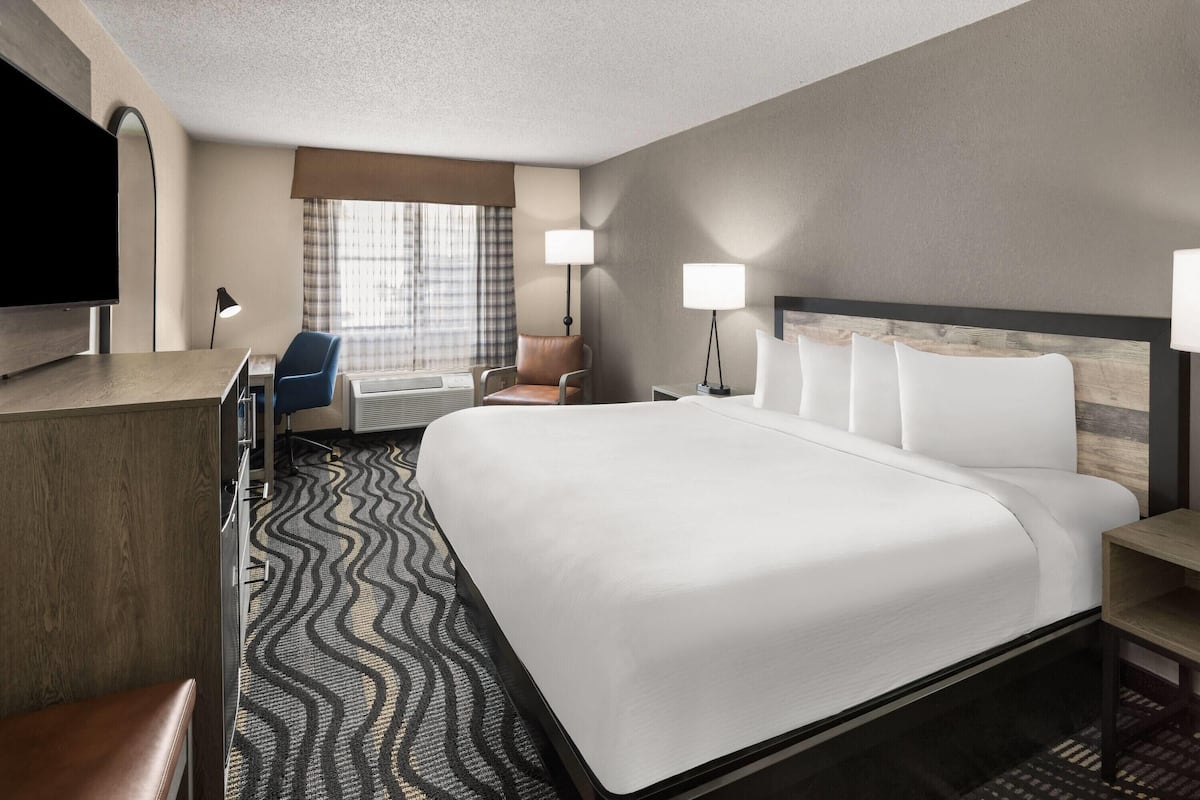 A hotel room with a large bed, a desk, a chair, a television, and two bedside lamps.