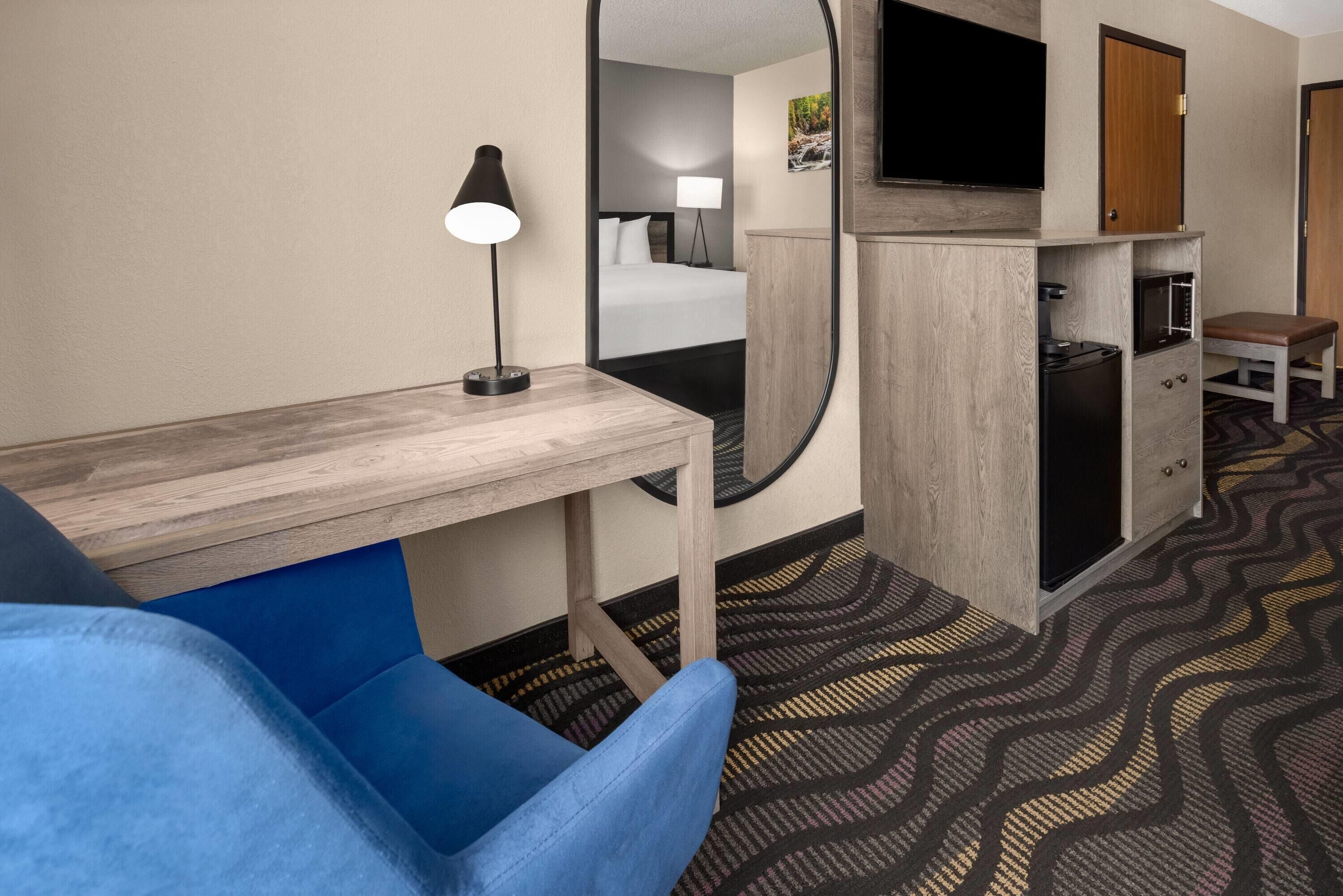 Ein Hotelzimmer mit Bett, Schreibtisch, Spiegel, Fernseher, Mikrowelle und einer kleinen Bank.