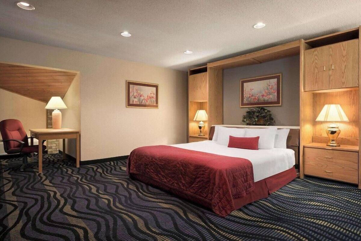 A hotel room with a large bed, a desk, a chair, and two nightstands with lamps.