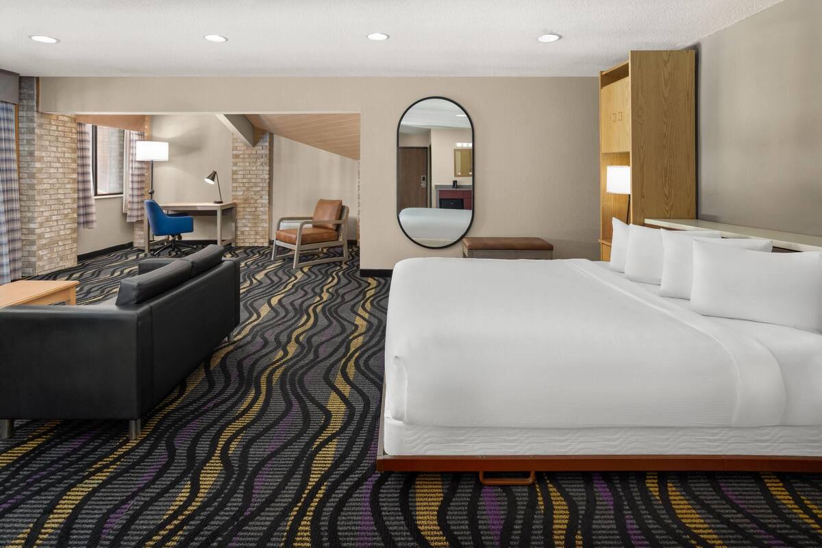 A hotel room with a large bed, a desk, a chair, a sofa, and a mirror.