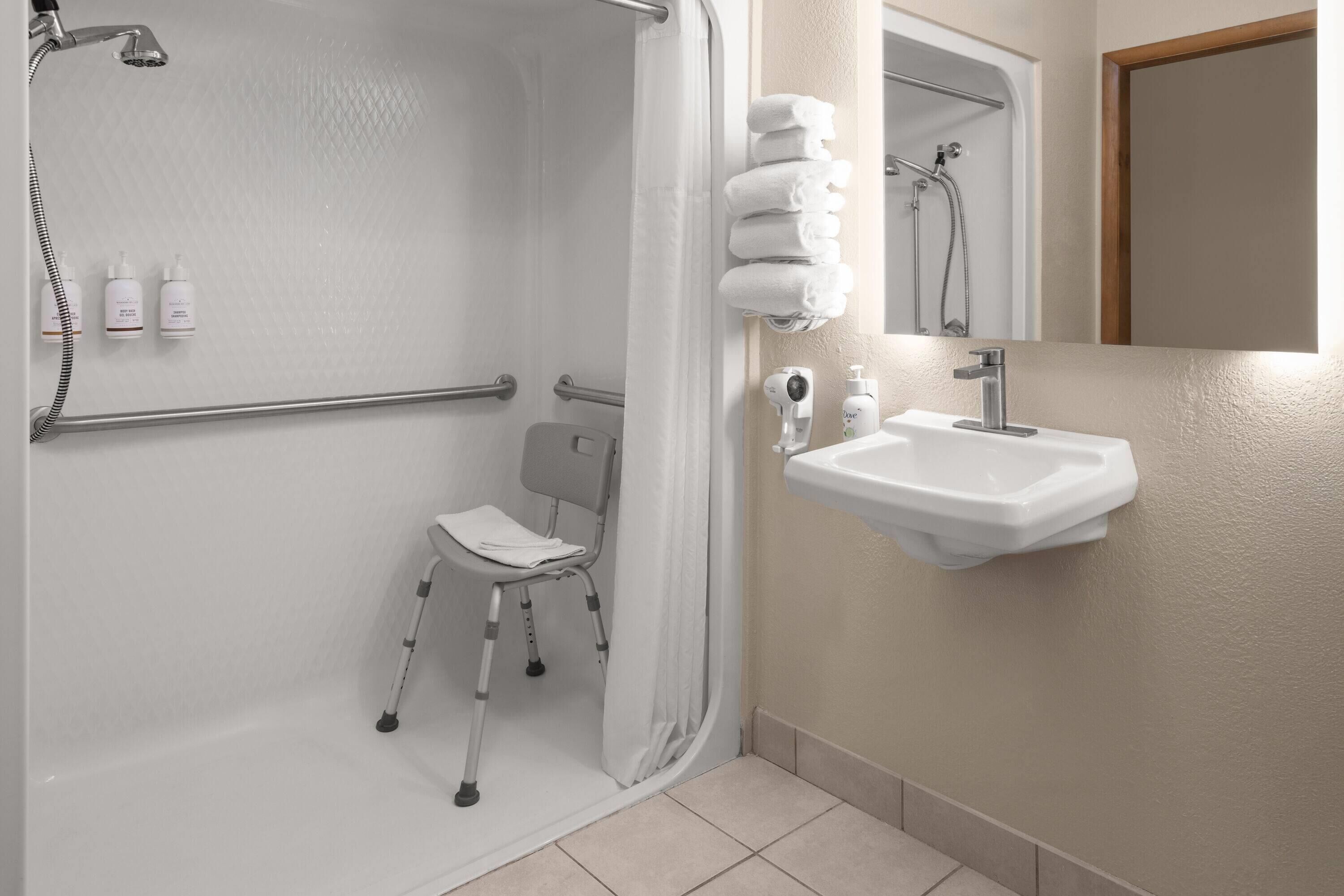 Un baño con ducha, una silla accesible para sillas de ruedas, un lavabo y un espejo.