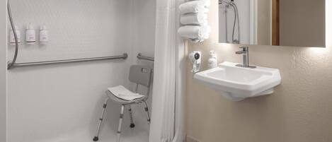 Un baño con ducha, una silla accesible para sillas de ruedas, un lavabo y un espejo.