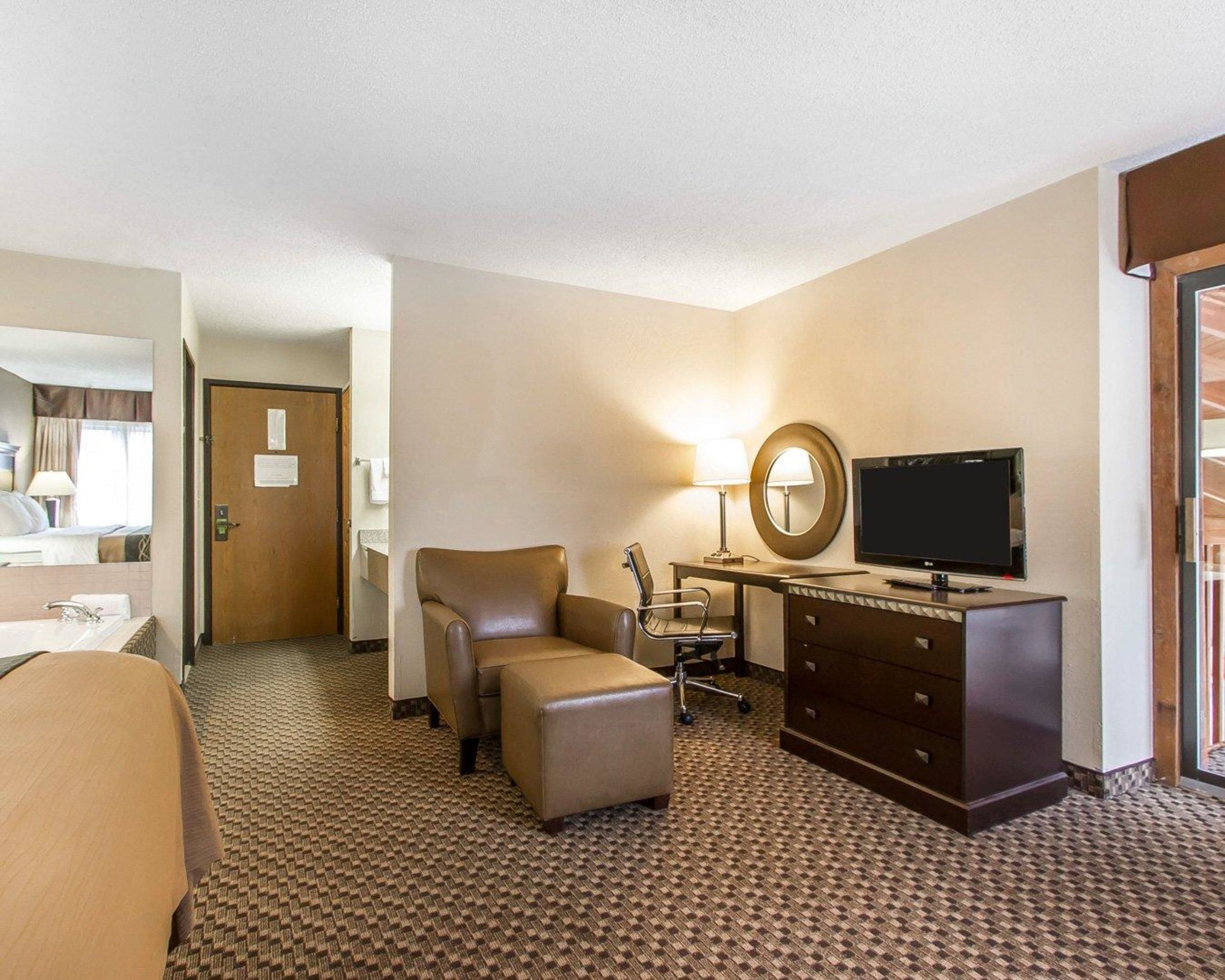A hotel room with a bed, a desk with a TV, a chair, a lamp, and a dresser.