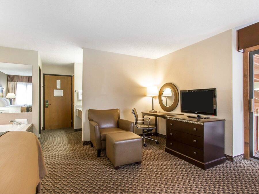 A hotel room with a bed, a desk with a TV, a chair, a lamp, and a dresser.