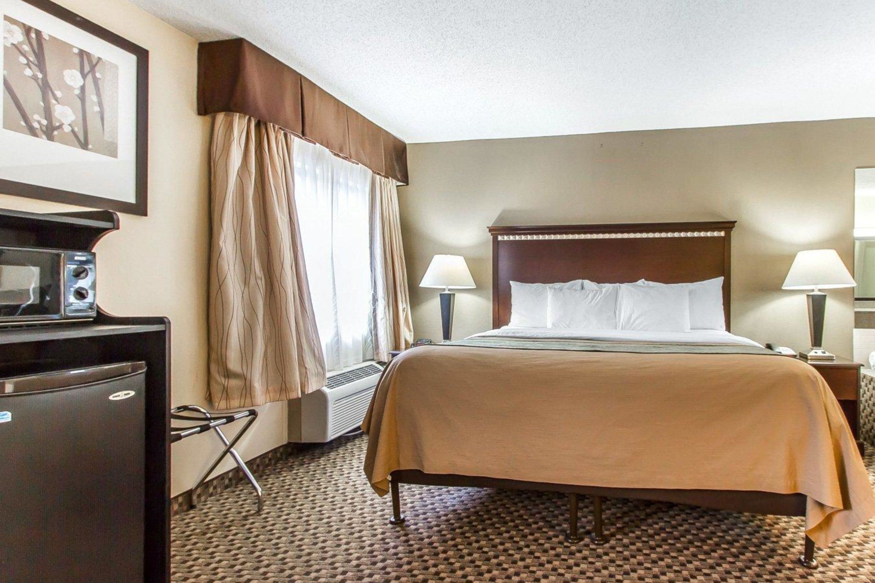 Ein Hotelzimmer mit einem Bett, zwei Nachttischlampen, einem Schreibtisch mit einem Radio und einem Fenster mit Vorhängen.