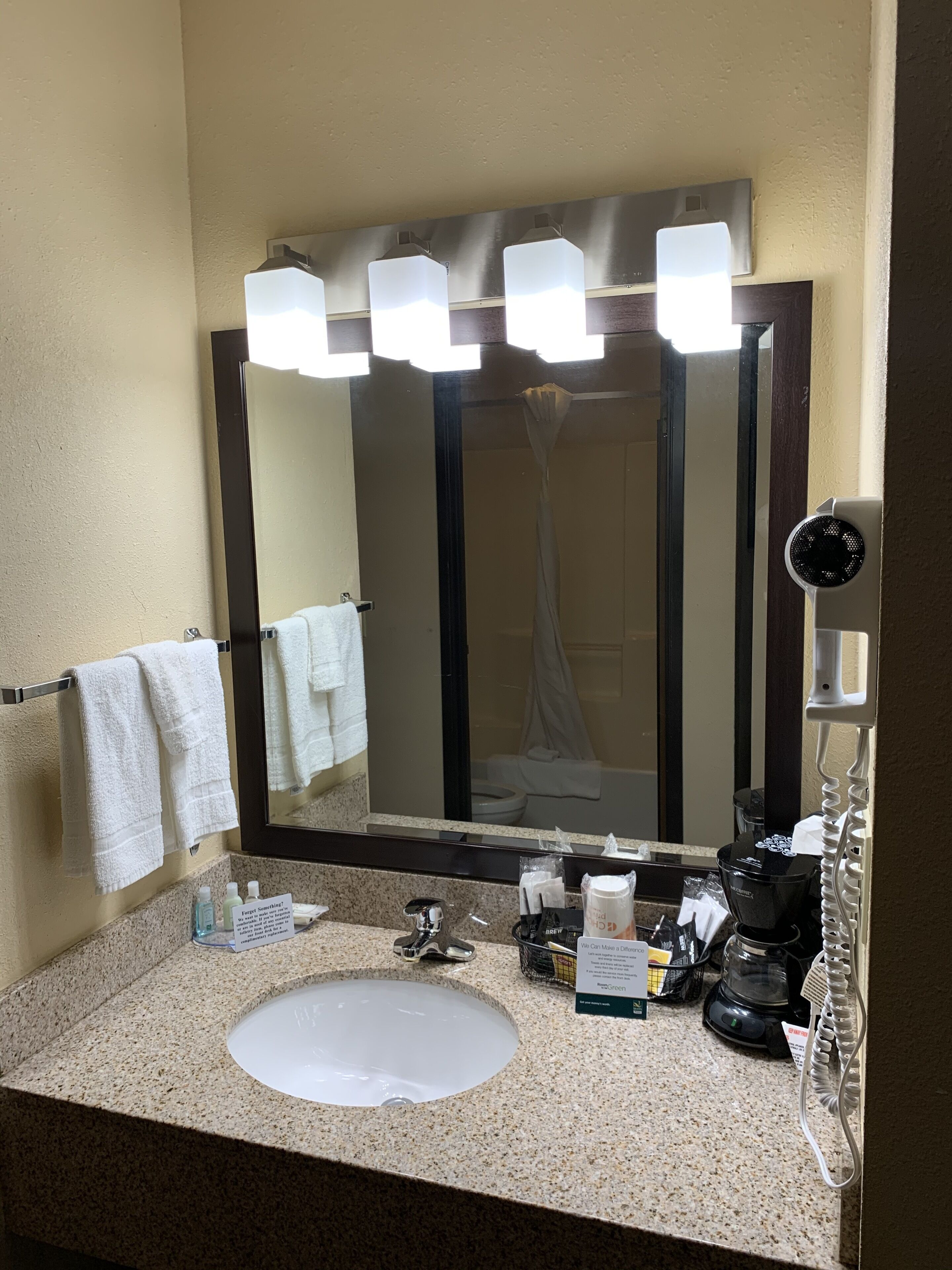 A bathroom with a large mirror, multiple lights, a sink, and a shower area.