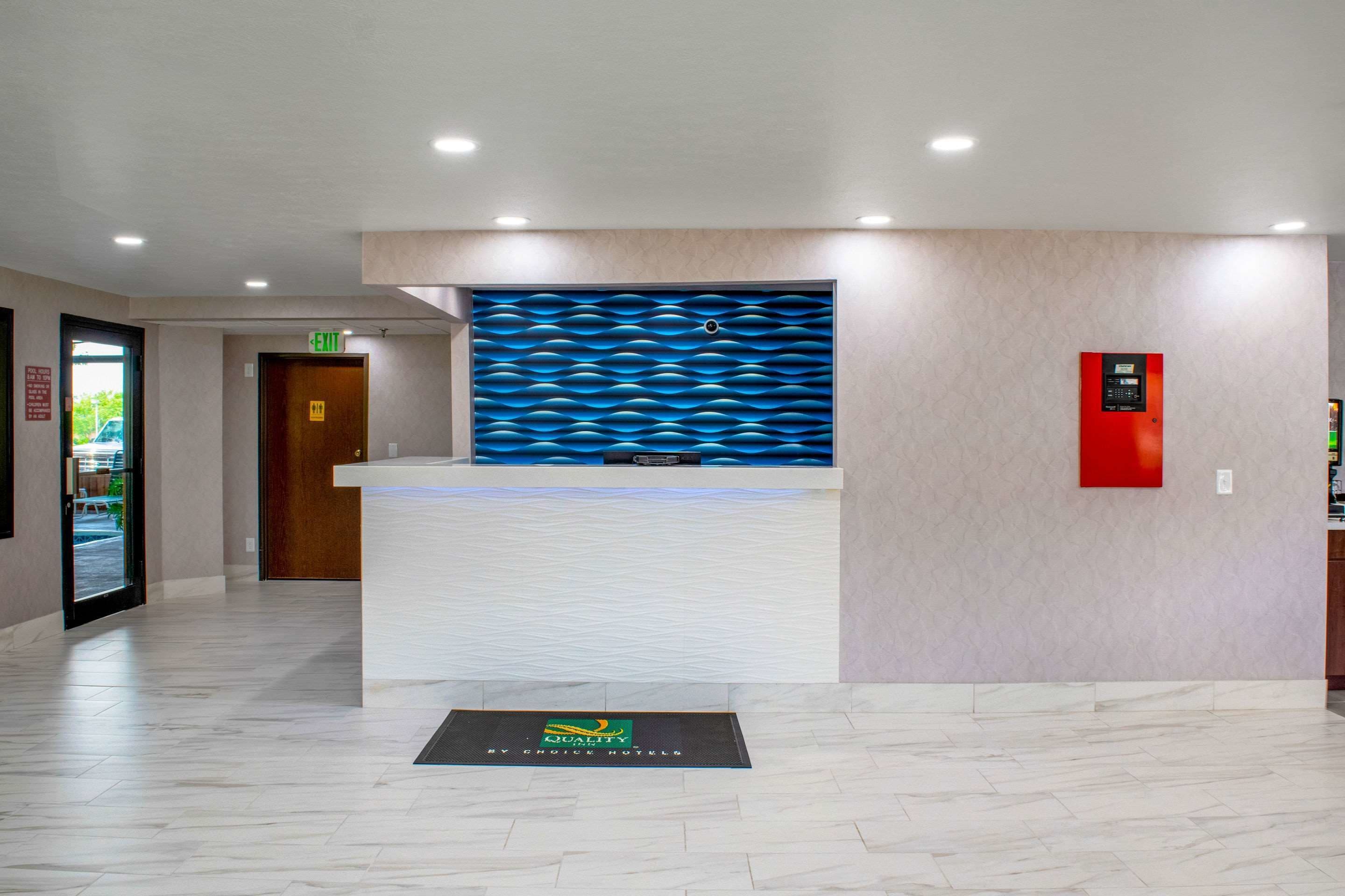 A reception area with a modern design, including a reception desk, a wall-mounted information panel, and a red emergency alarm box.