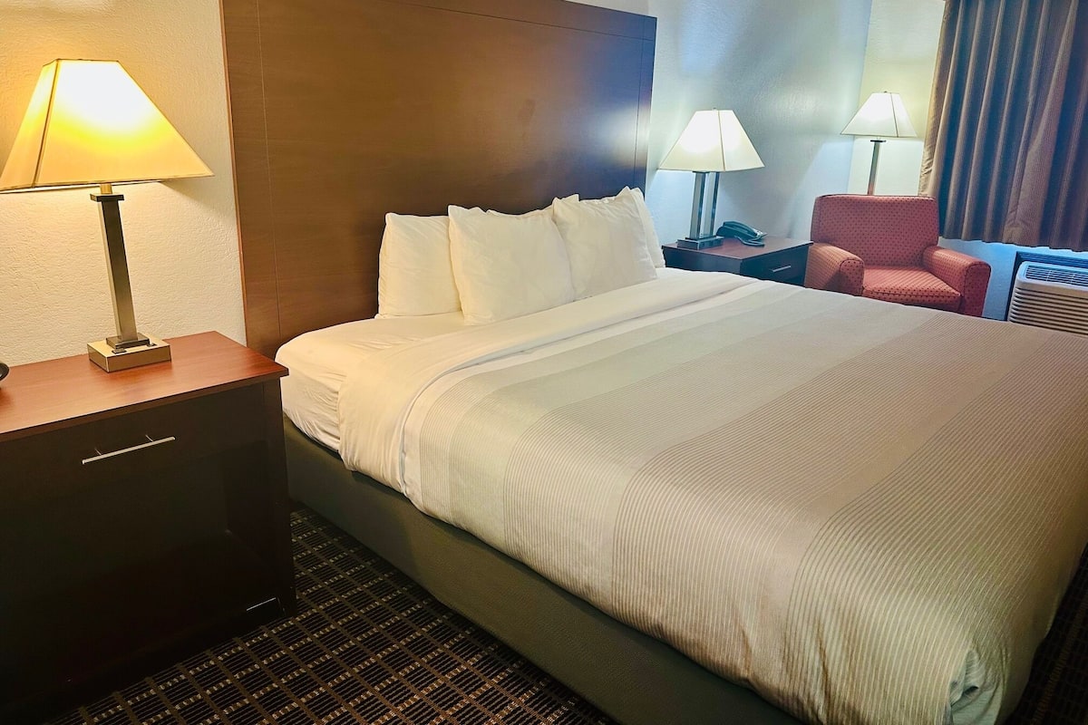 Quarto de hotel com uma cama grande, duas luminárias de cabeceira, uma cadeira e uma escrivaninha com telefone.
