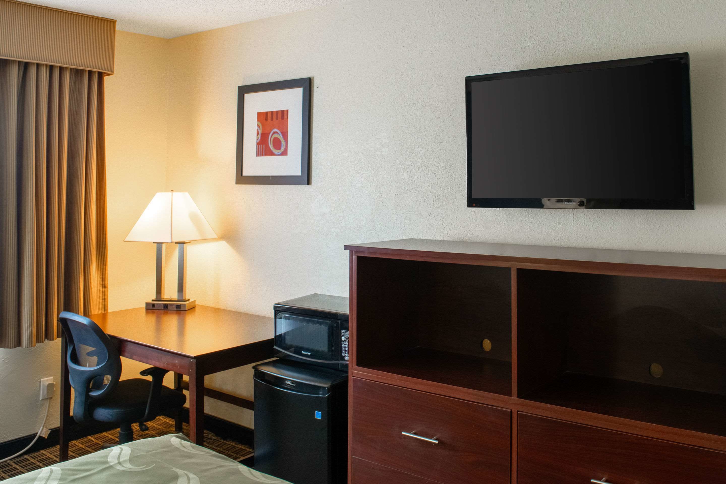Habitación de hotel con cama, escritorio con lámpara, microondas, televisor y armario.