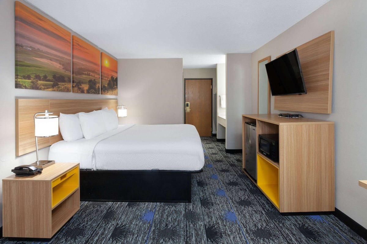 A hotel room with a bed, bedside table, lamp, TV, and artwork on the wall.