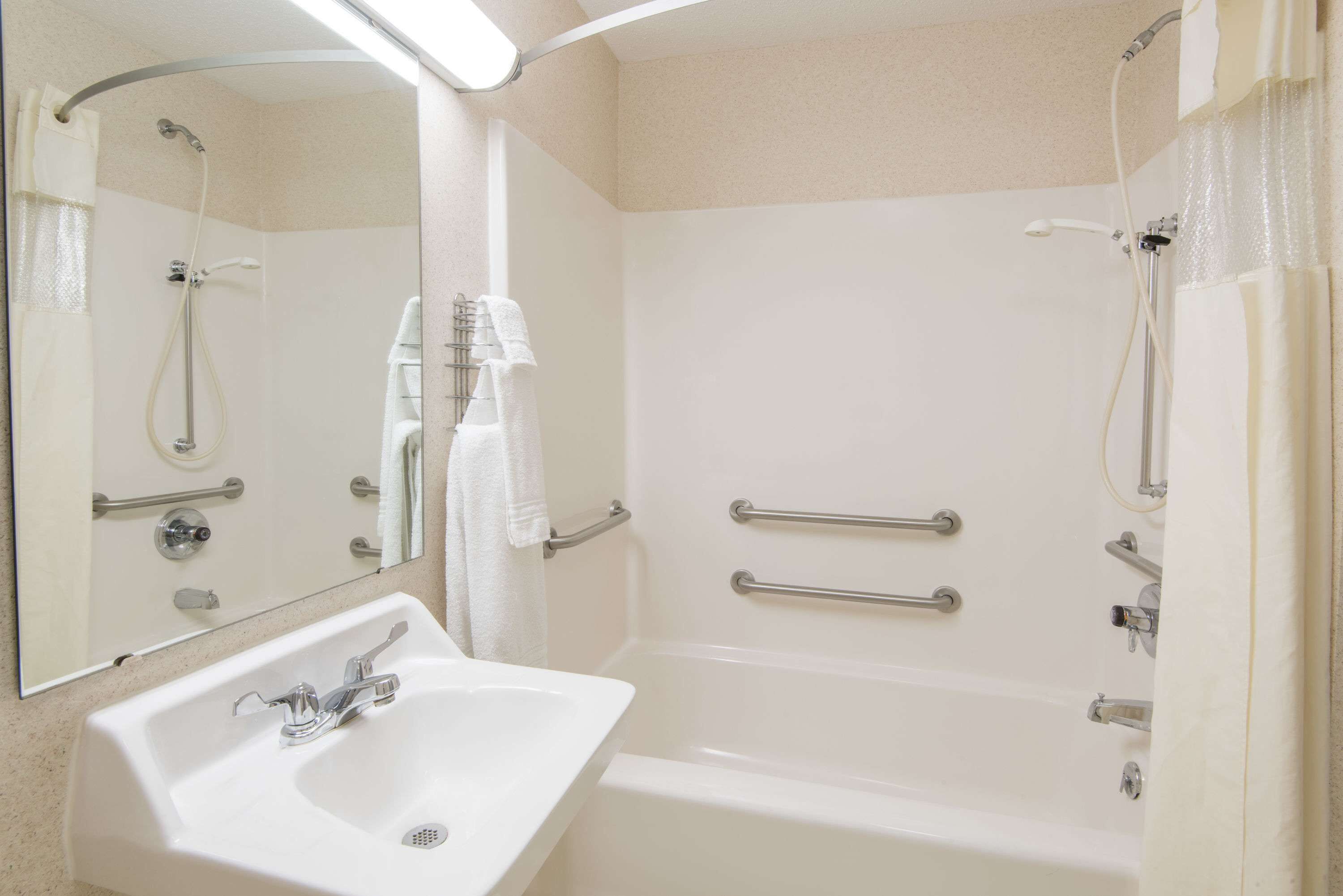 Un baño con lavamanos, espejo, ducha y barras de apoyo.