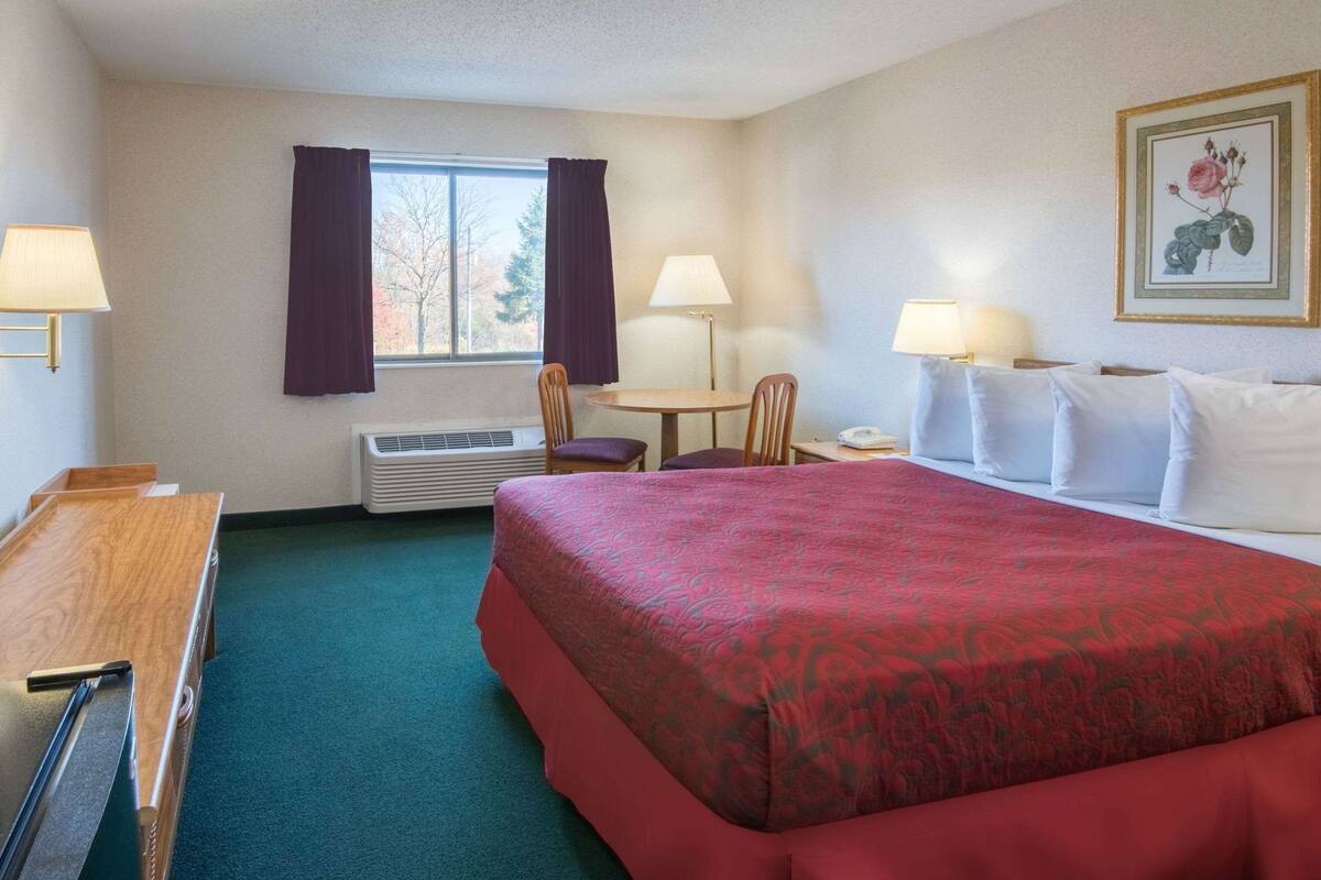 A hotel room with a bed, a desk, a chair, a table, and a window with curtains.