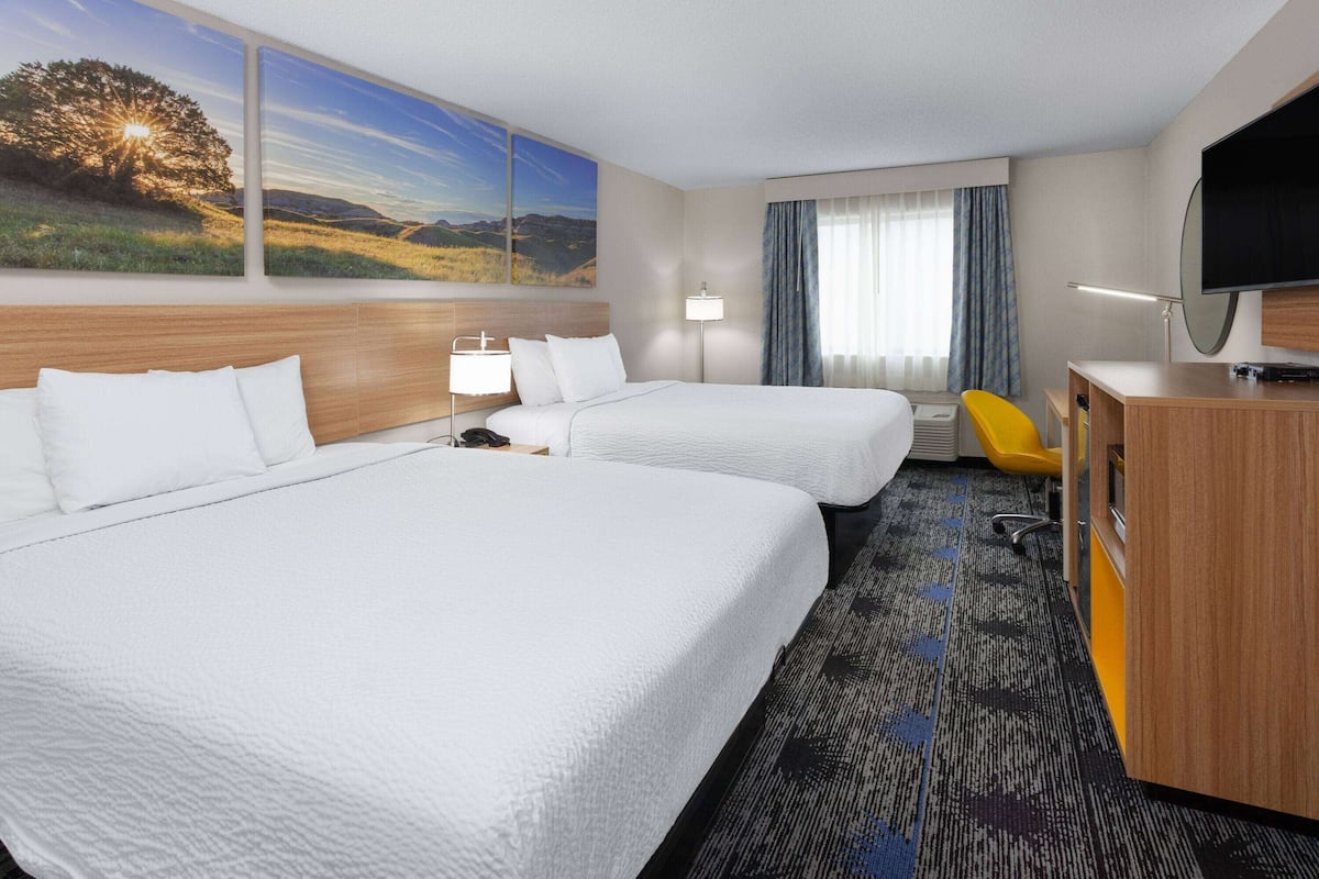A hotel room with two beds, a desk, a TV, and a window with curtains.