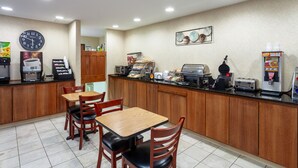 Un área de desayuno con mesas y sillas de madera, una cafetera, un tostador y un reloj en la pared.