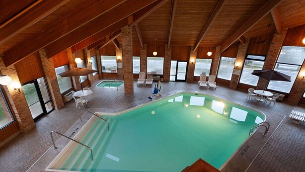 Una piscina interior con techo de madera, paredes de ladrillo y grandes ventanales.