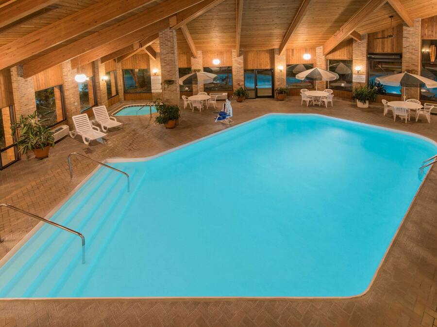 An indoor swimming pool with lounge chairs and umbrellas, surrounded by wooden walls and large windows.