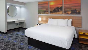 A hotel room with a large bed, a round mirror, a sink, and three sunset paintings on the wall.