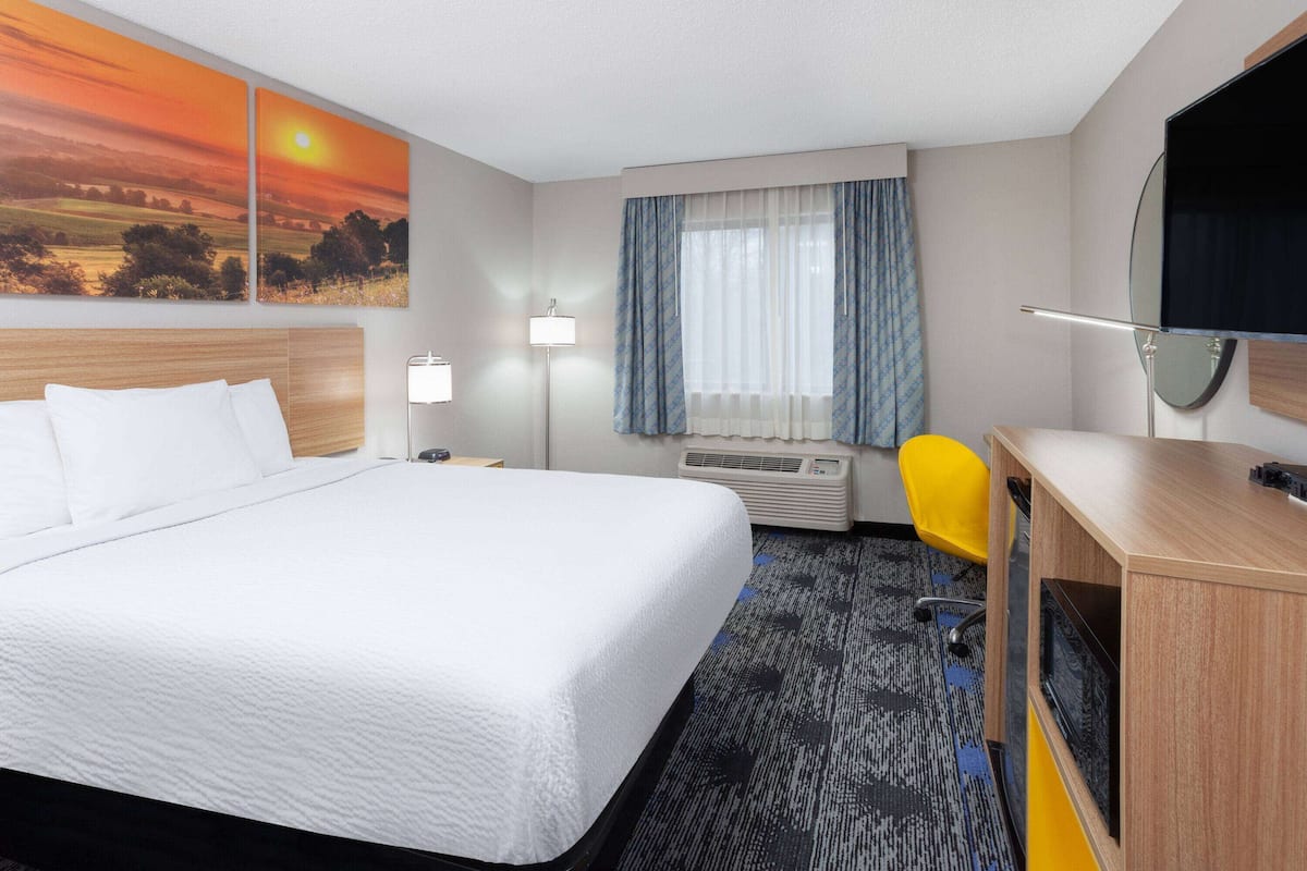A hotel room with a large bed, a desk, a chair, a TV, and a window with curtains.