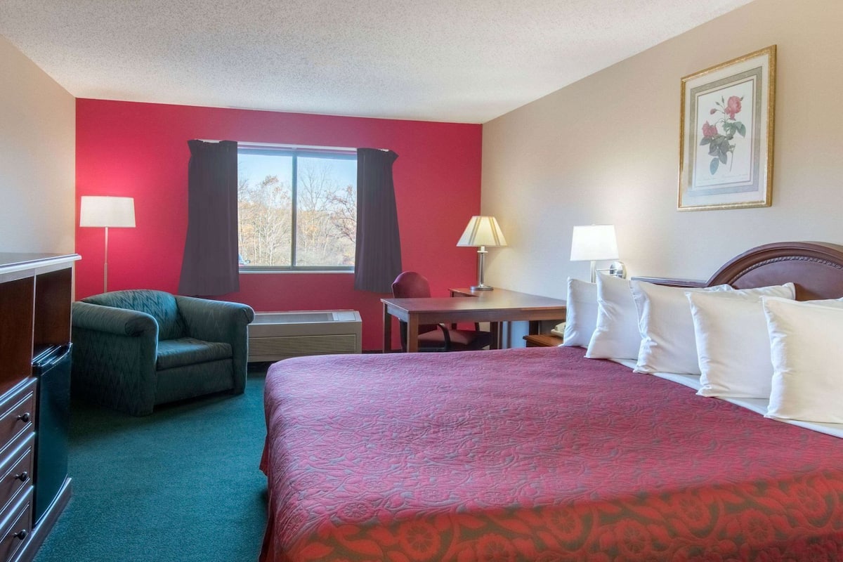 A hotel room with a bed, a desk, a chair, a dresser, and a window with curtains.