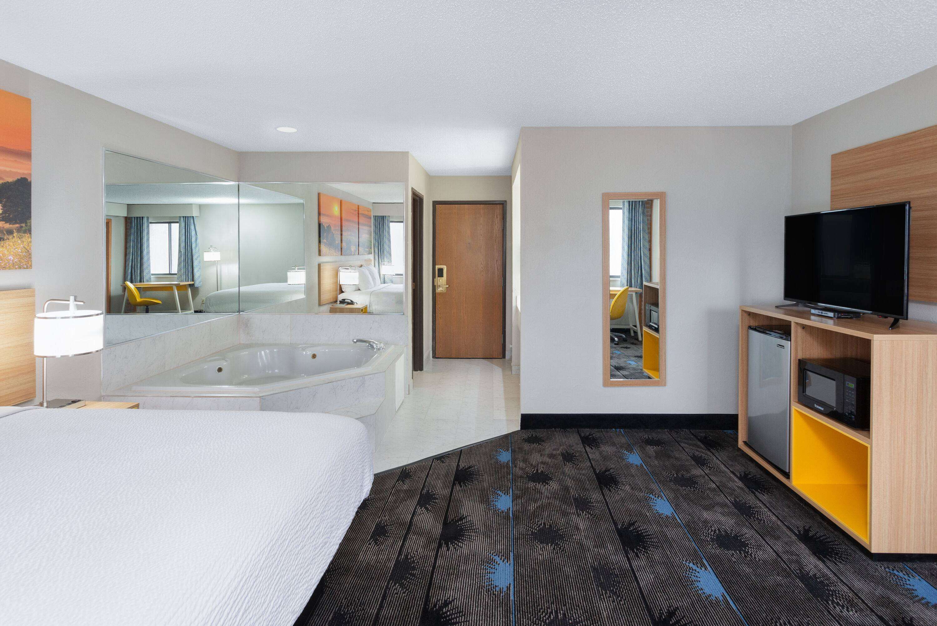 Hotelkamer met een groot bed, een aparte badkamer met bad, een televisie en een kleine koelkast.