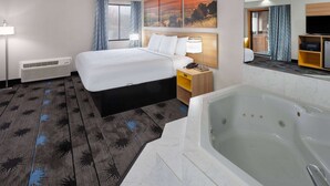 Habitación de hotel con una cama grande, un baño independiente con bañera, un escritorio con lámpara y un televisor en un estante.