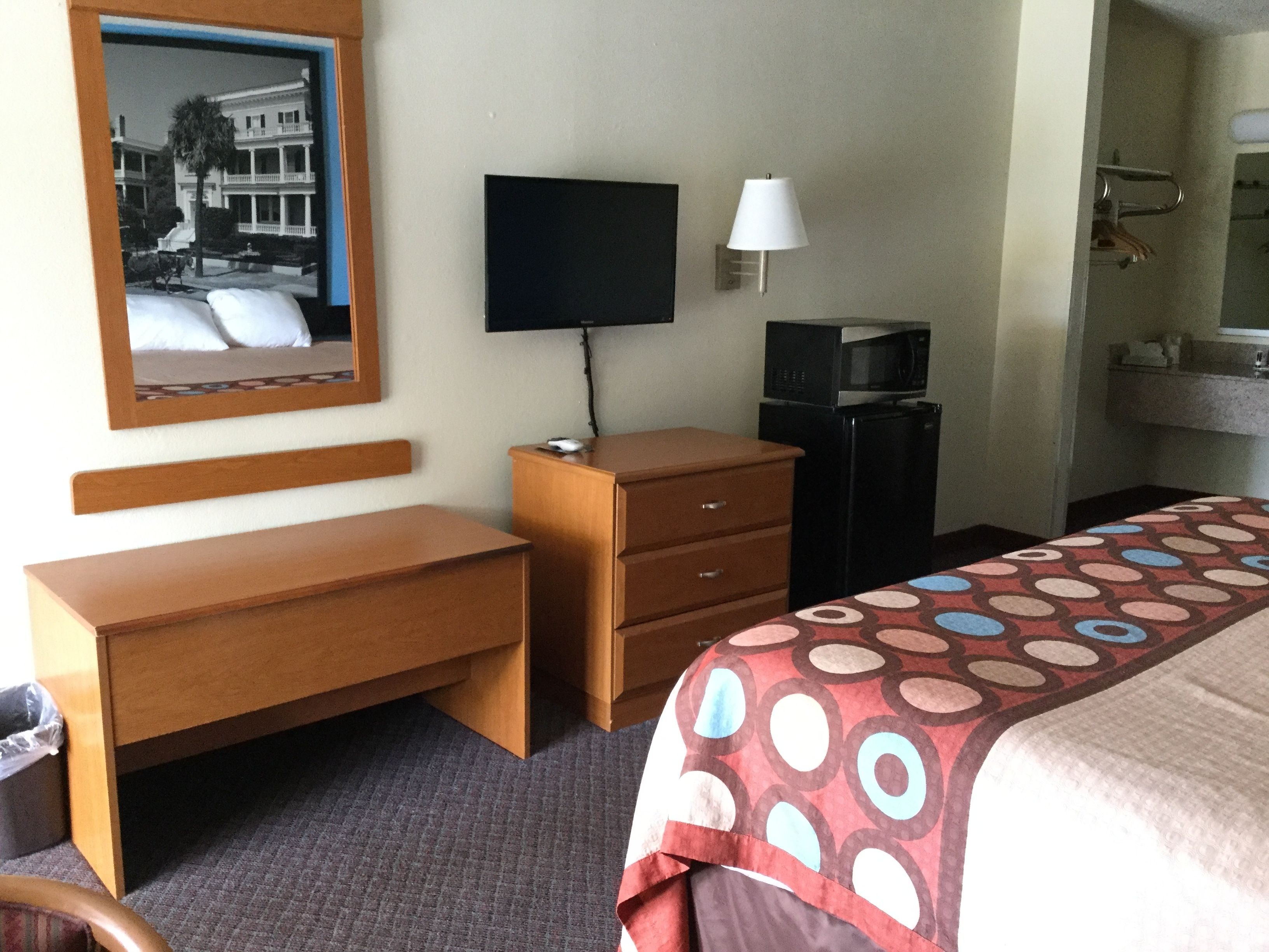 A hotel room with a wooden desk, a television, a small refrigerator, and a bed with a patterned bedspread.