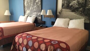 Habitación de hotel con dos camas, cada una con una colcha estampada en rojo y beige, un cuadro grande en la pared y una mesita de noche con lámpara y teléfono.