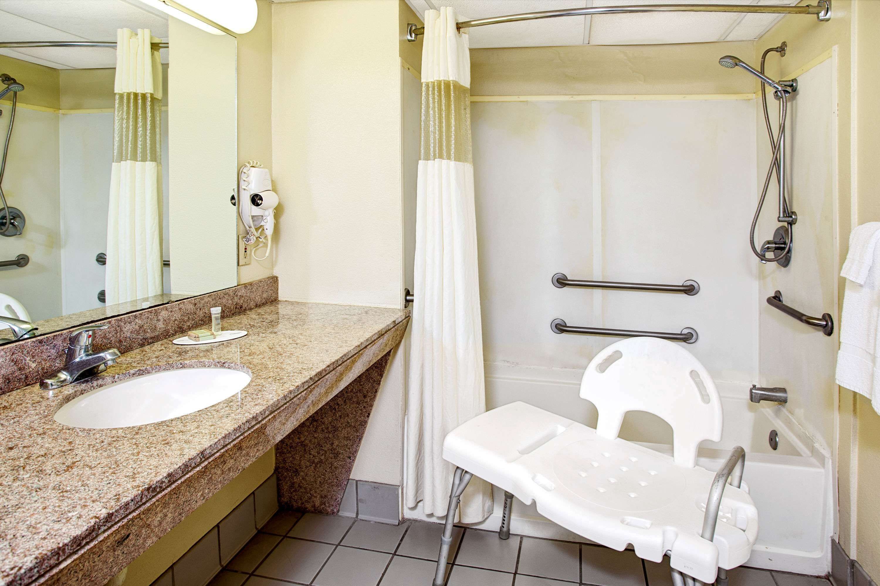 Baño con lavamanos, espejo, ducha y un banco accesible para sillas de ruedas.