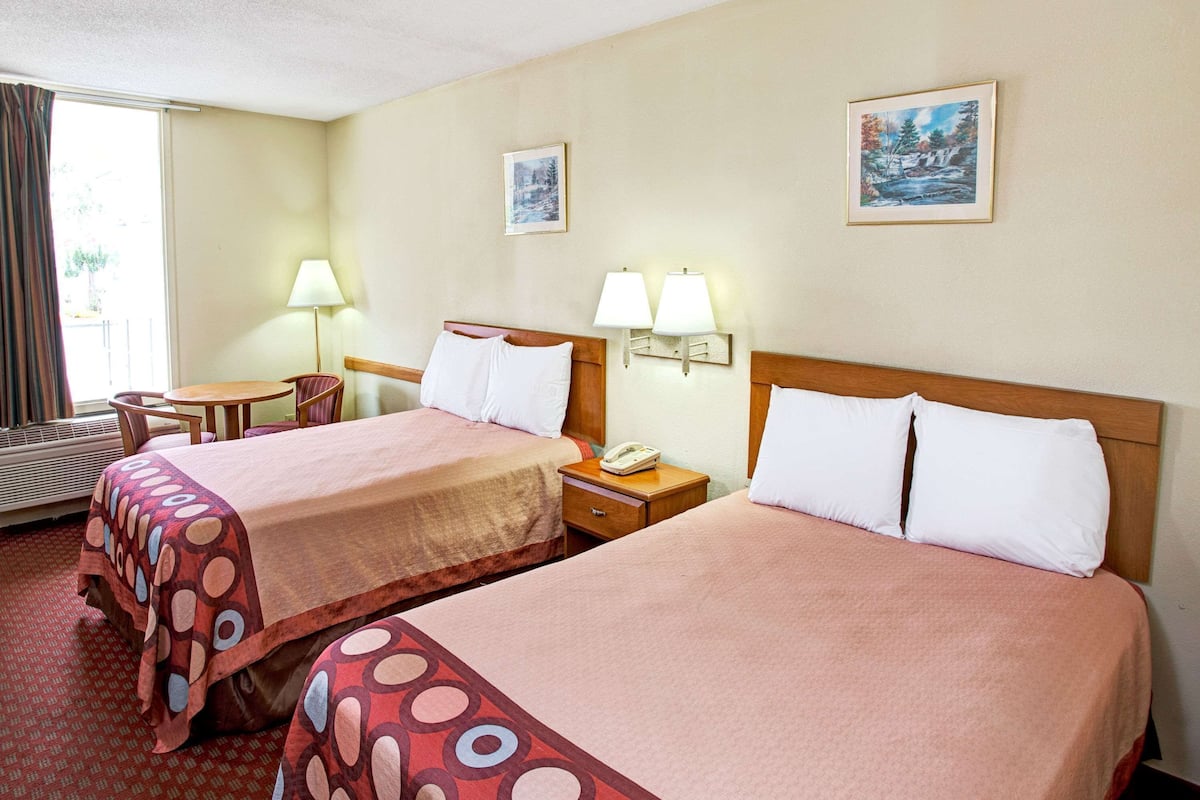 Habitación de hotel con dos camas, un escritorio, una silla, una lámpara y dos lámparas de pared.