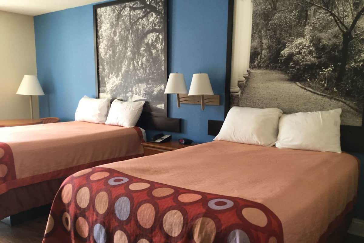Habitación de hotel con dos camas, un cuadro grande enmarcado y una mesita de noche con lámparas.