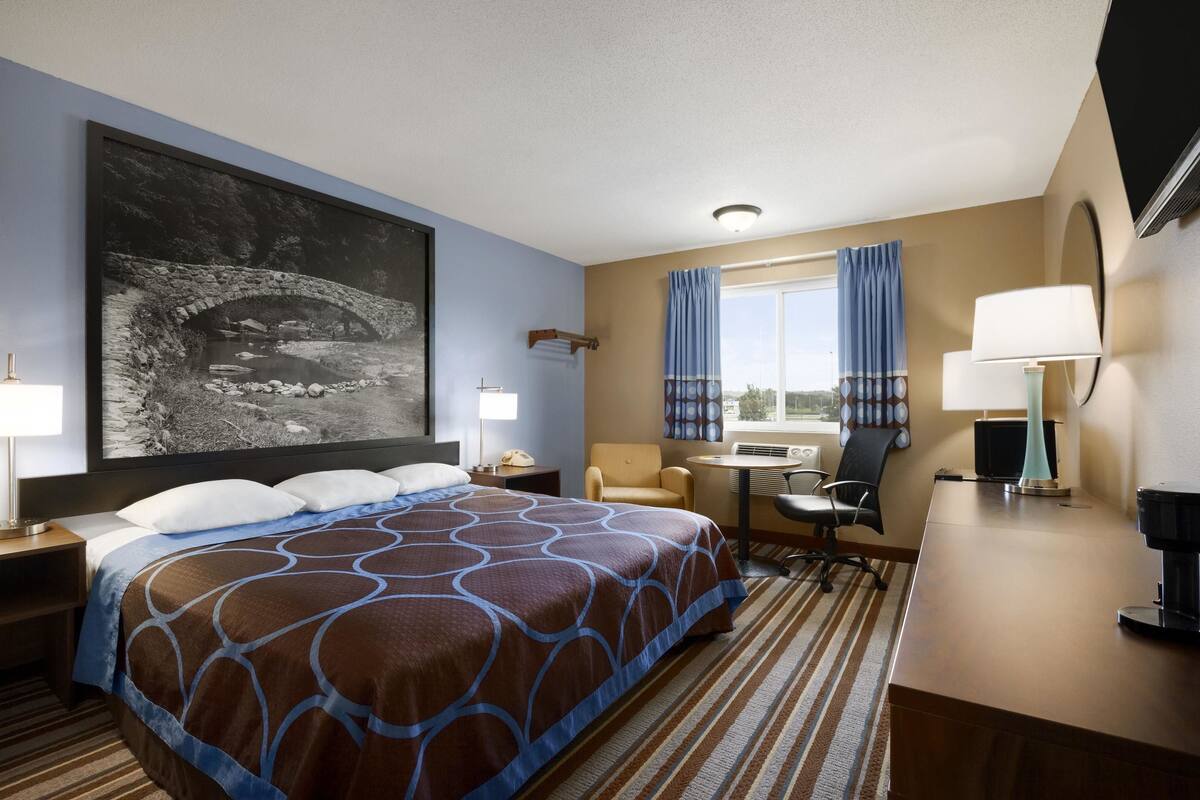 A hotel room with a large bed, a desk, a chair, a TV, and a window with curtains.
