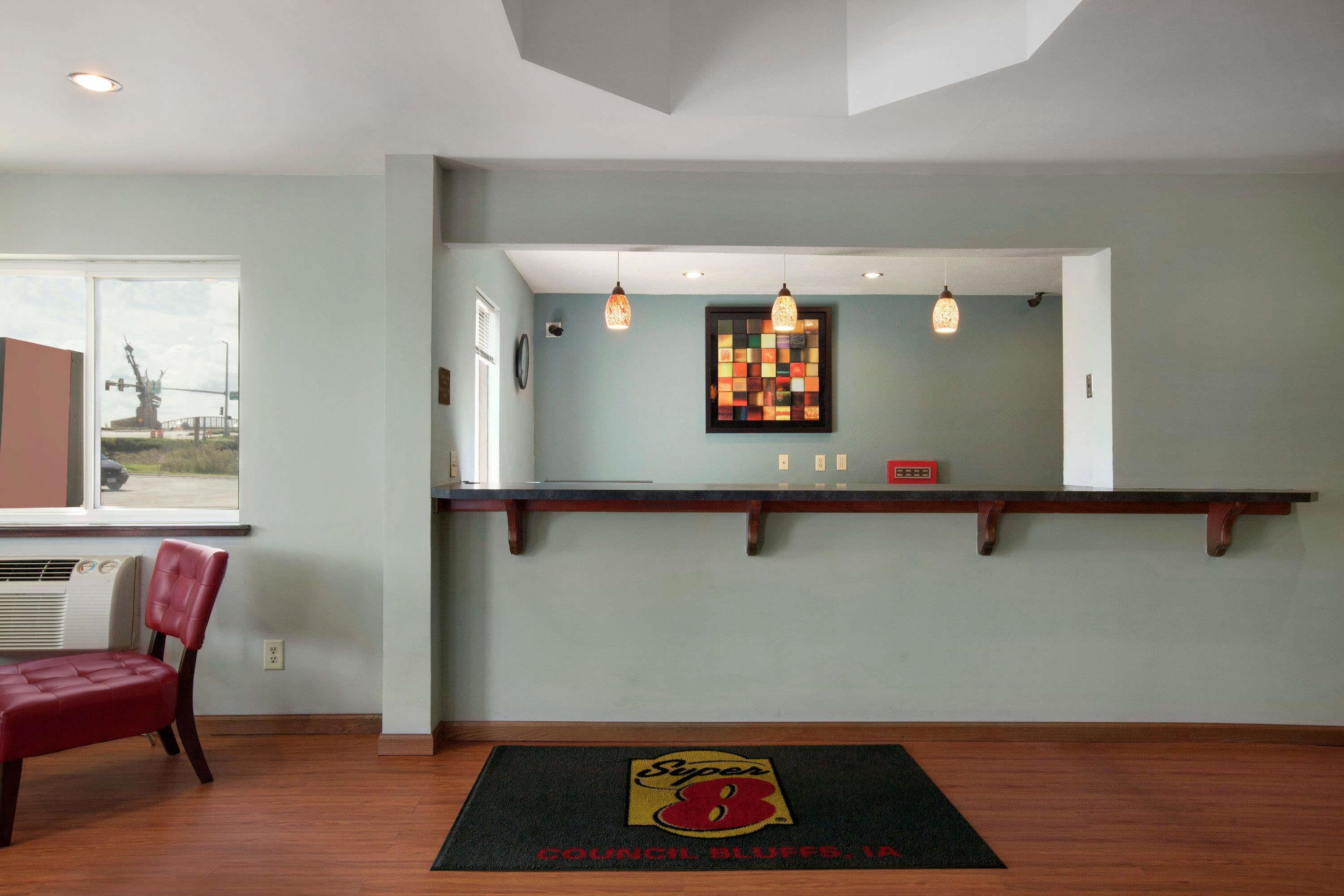 A lobby with a reception desk, a chair, a colorful artwork, and a logo on the floor mat.