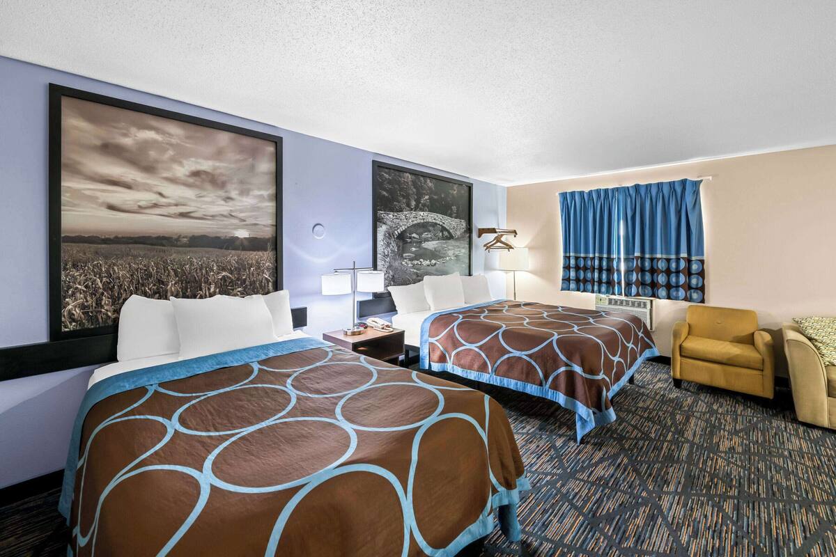 A hotel room with two beds, a desk, a chair, and a large window with curtains.