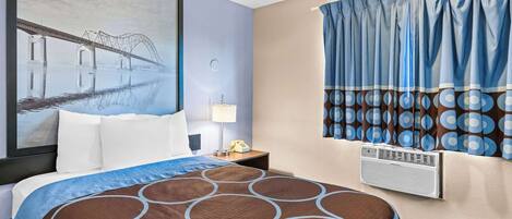Una habitación de hotel con una cama grande, una mesita de noche con lámpara, aire acondicionado instalado en la pared y una ventana con cortinas.