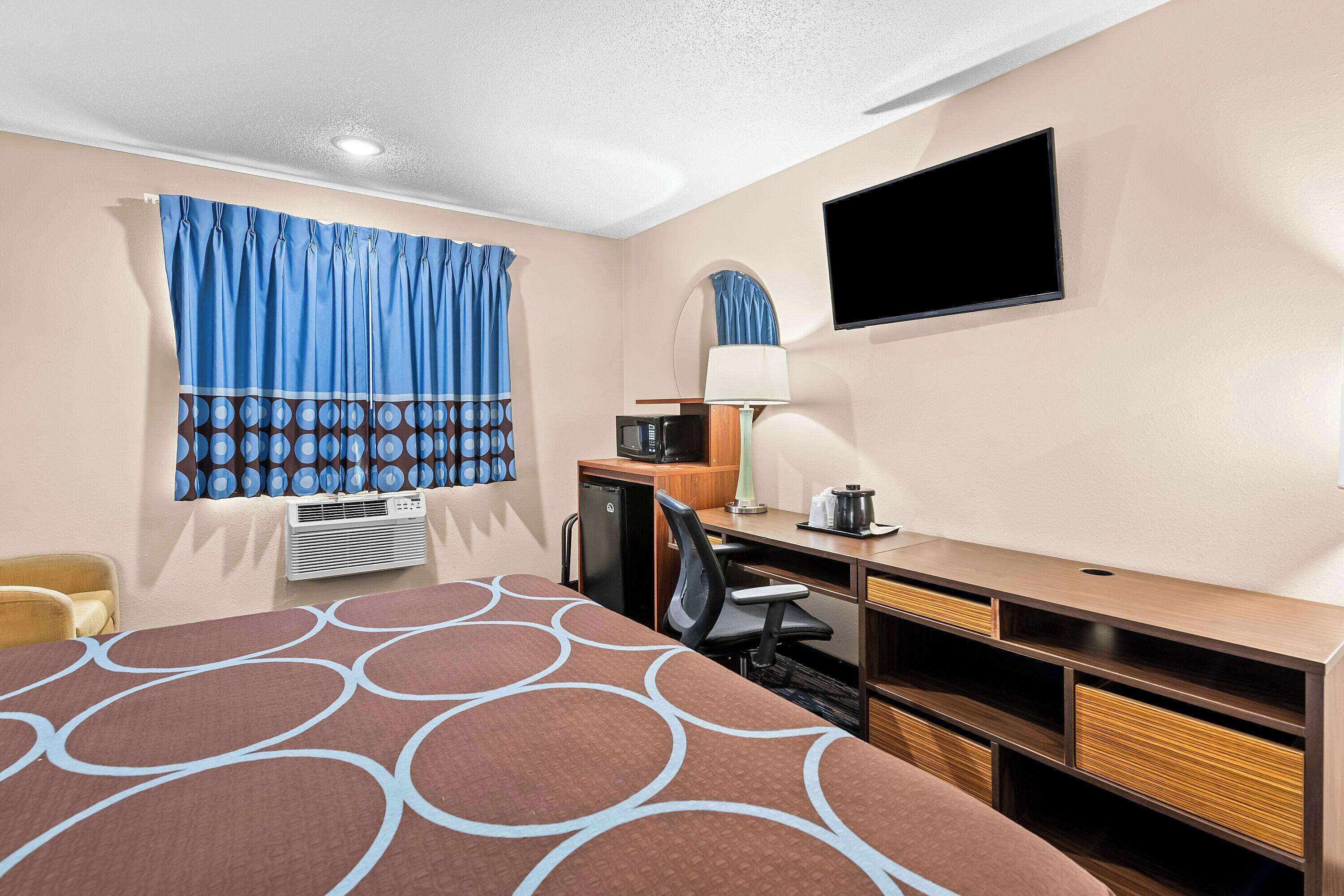 Une chambre d’hôtel équipée d’un lit, d’un bureau, d’une chaise, d’une télévision et d’une fenêtre avec des rideaux.