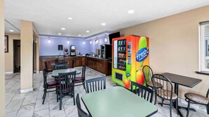 A restaurant with a vending machine, tables, chairs, and a kitchen area. - Super 8 by Wyndham Council Bluffs IA Omaha NE Area (Council Bluffs)