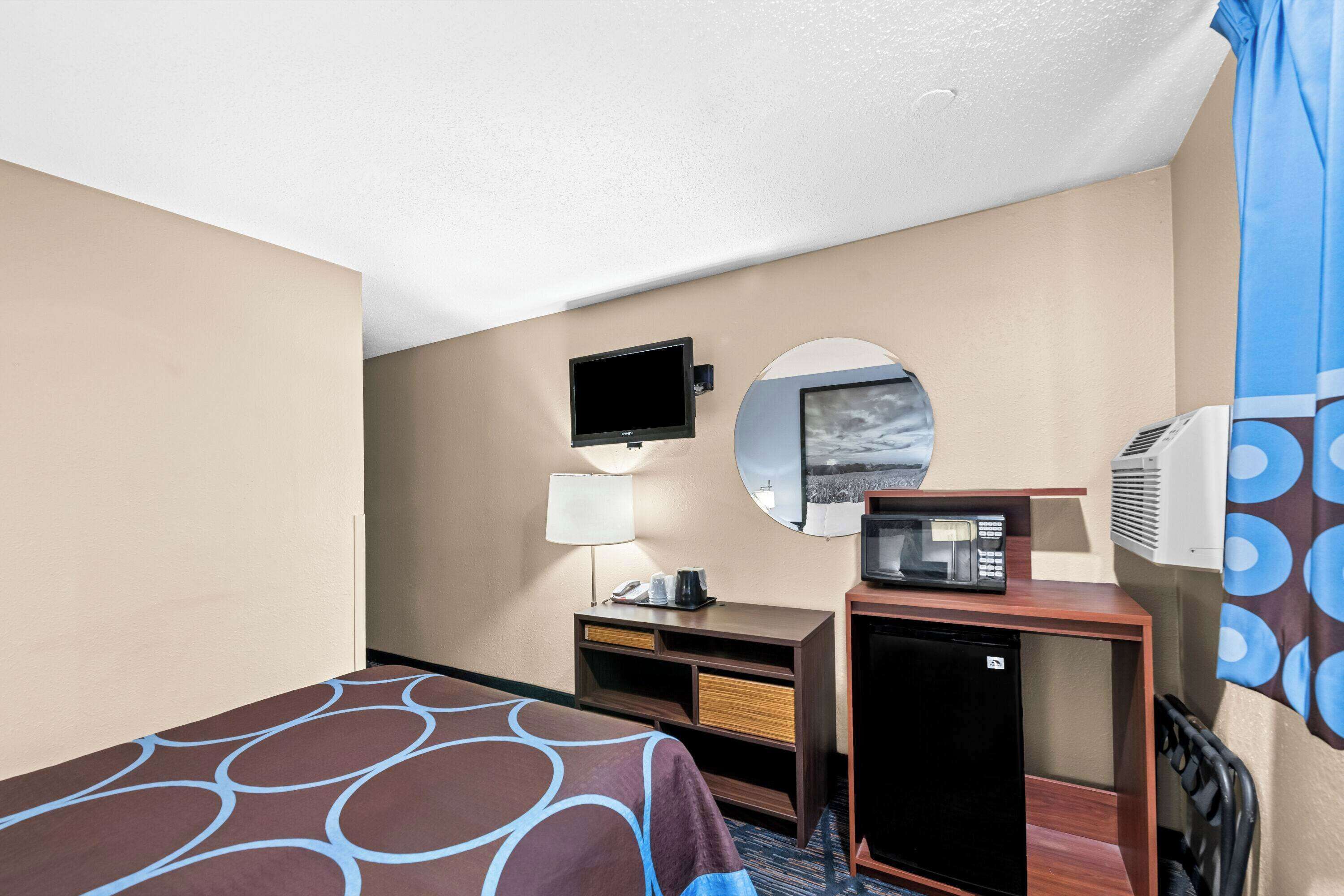Une chambre d’hôtel équipée d’un lit, d’un bureau avec une lampe, d’une télévision, d’un four à micro-ondes et d’un climatiseur.