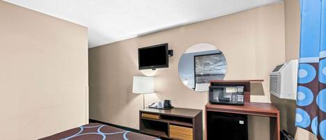 Une chambre d’hôtel équipée d’un lit, d’un bureau avec une lampe, d’une télévision, d’un four à micro-ondes et d’un climatiseur.