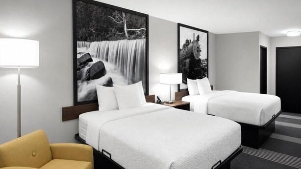 Habitación de hotel con dos camas, un sofá, una lámpara y dos cuadros grandes en la pared.