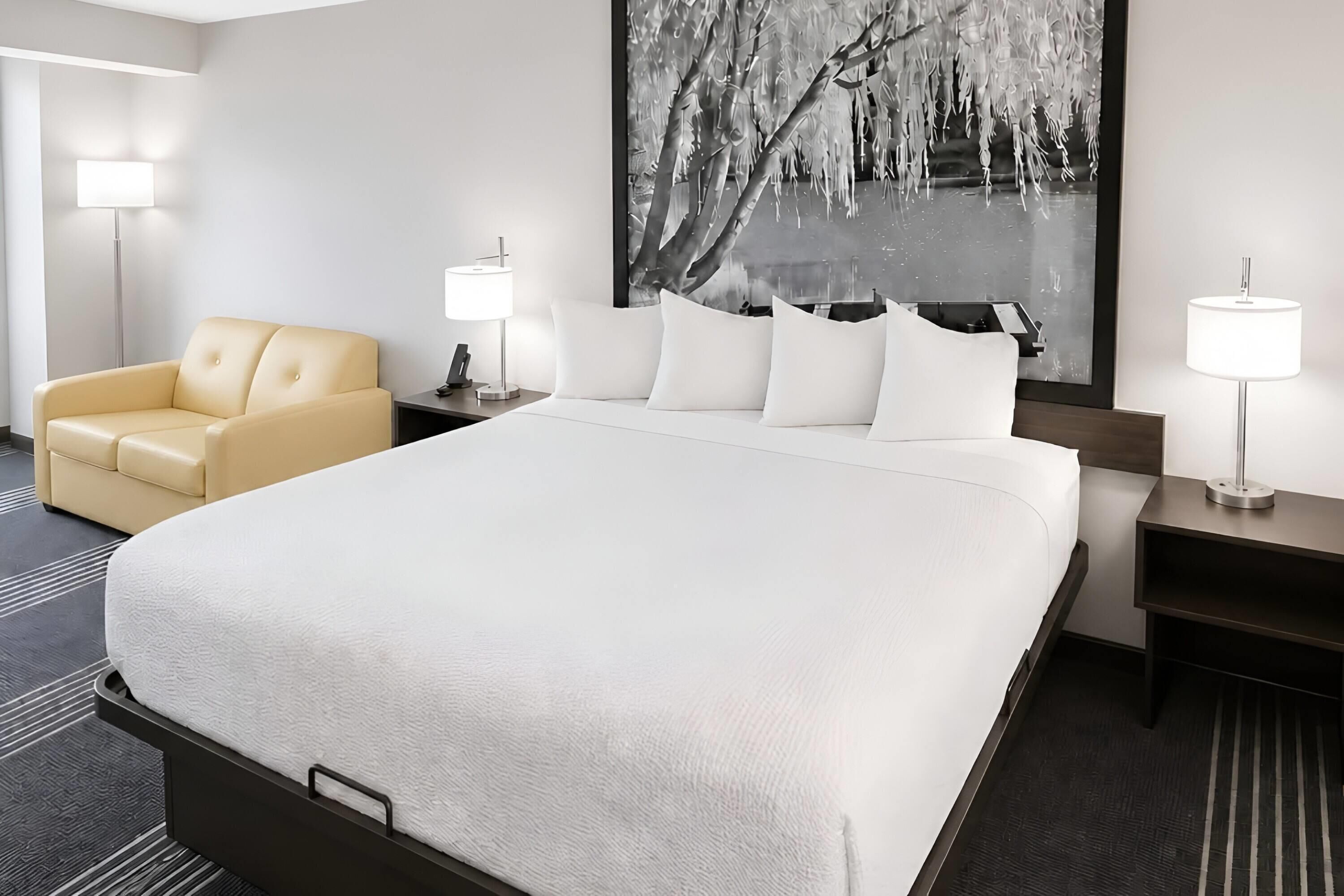 Ein Hotelzimmer mit einem großen Bett, einer Couch, zwei Nachttischen mit Lampen und einem großen gerahmten Bild an der Wand.