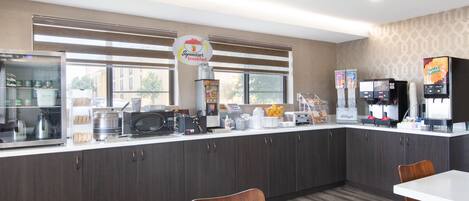 A modern kitchen area with a breakfast bar, microwave, coffee machine, and various food items.