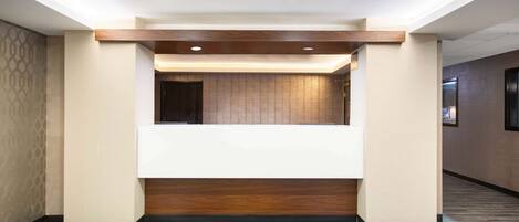 A hotel reception area with a reception desk, a wooden accent wall, and a reception mat with the hotel's logo.