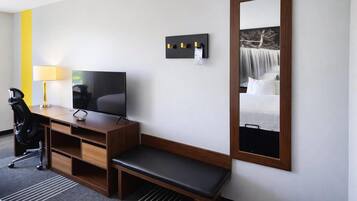 Habitació d'hotel amb escriptori de fusta, televisió, una panxa, un mirall i una làmpada fixada a la paret.
