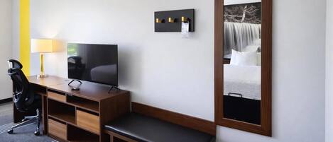 Habitació d'hotel amb escriptori de fusta, televisió, una panxa, un mirall i una làmpada fixada a la paret.
