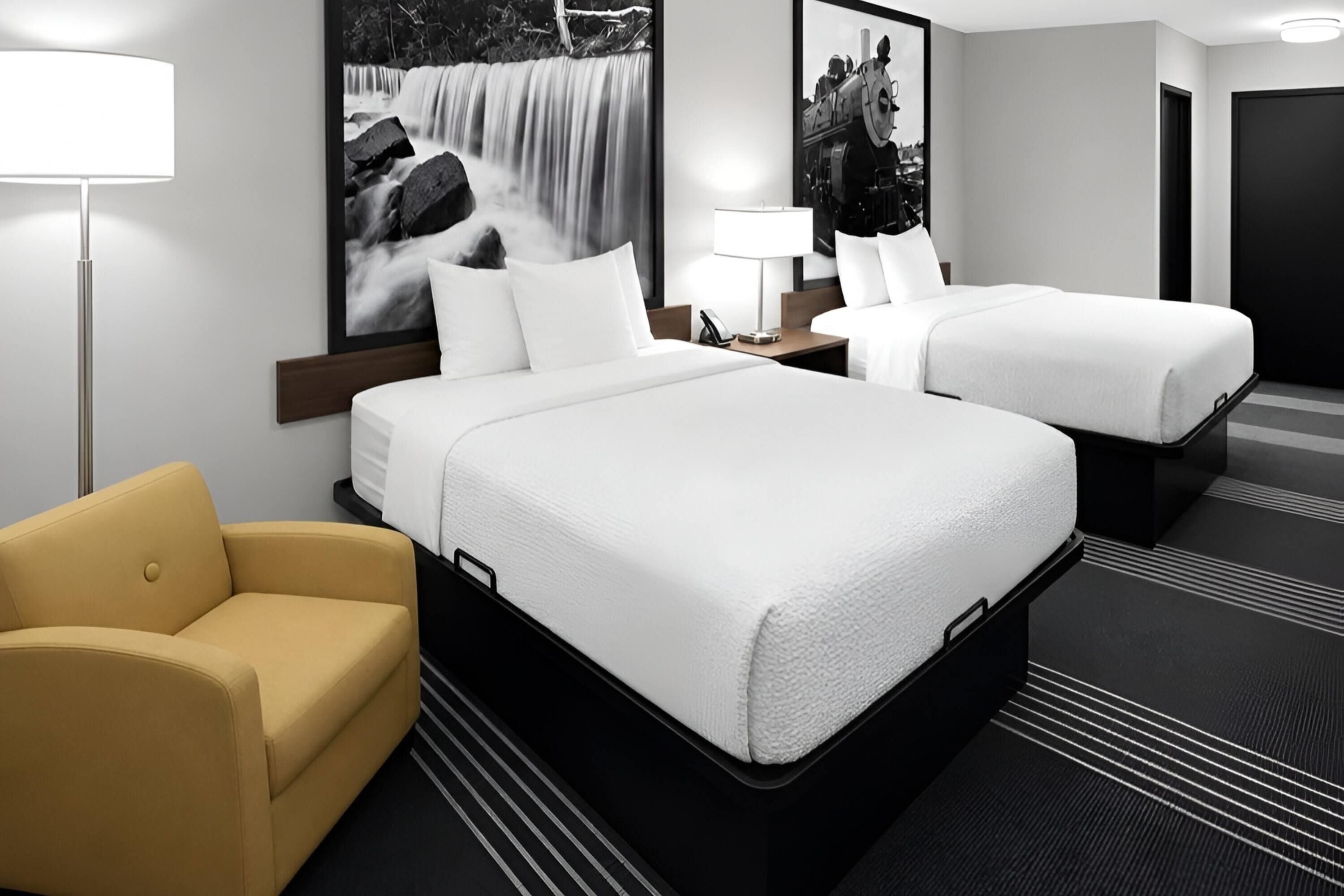 Une chambre d’hôtel avec deux lits, un canapé, une table de chevet, une lampe et un grand tableau encadré représentant une cascade.
