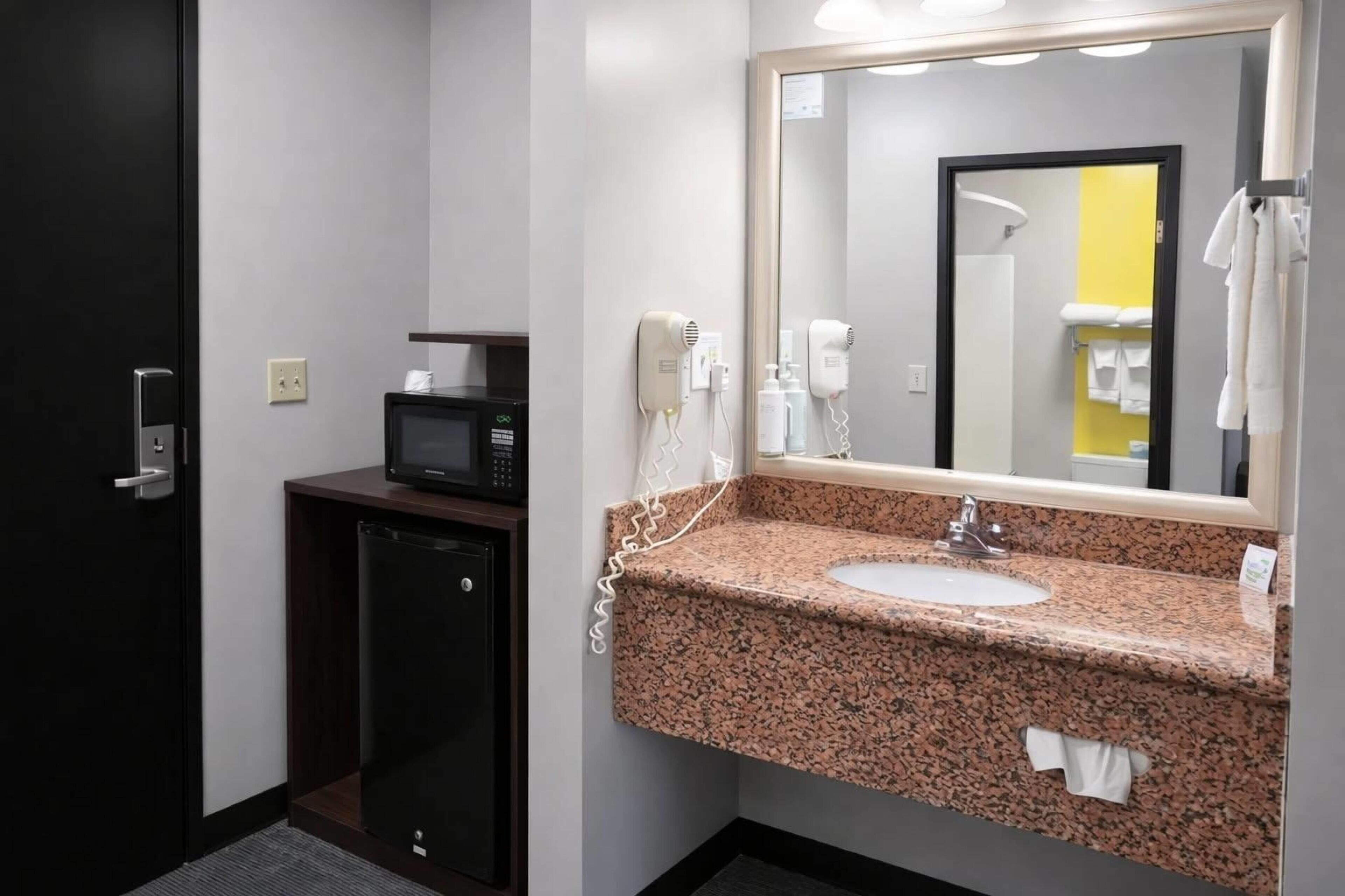 A hotel bathroom with a granite sink, a mirror, a microwave, and a hairdryer.